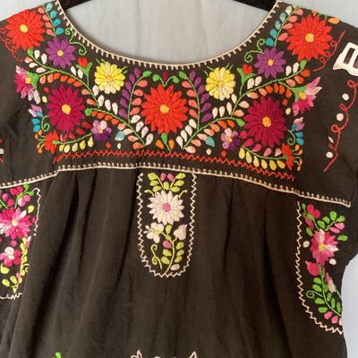 Sale Photo Thumbnail #393: Black short-sleeve embroidered Mexican huipil tunic dress featuring colorful floral embroidery across the neckline, chest, and front lower panel. Features a scoop neckline with stitch details and side vents at the hem. Measures approximately 35 inches in 