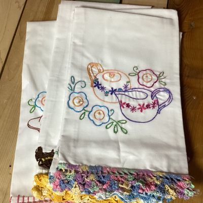 Sale Photo Thumbnail #340: Set of 4 vintage white cotton tea towels featuring colorful hand-embroidered kitchen and dining motifs including teapots, teacups, utensils, a covered dish, and floral accents. Each towel is finished along the bottom edge with hand-crocheted trim in vario