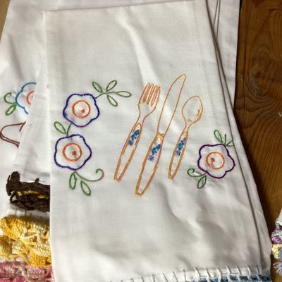 Sale Photo Thumbnail #338: Set of 4 vintage white cotton tea towels featuring colorful hand-embroidered kitchen and dining motifs including teapots, teacups, utensils, a covered dish, and floral accents. Each towel is finished along the bottom edge with hand-crocheted trim in vario