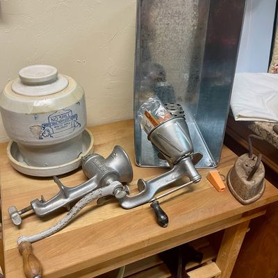 Sale Photo Thumbnail #135: Collection of vintage kitchenware including a White Hall Pottery Works 'No Spill' stoneware crock, two cast-iron hand-crank meat grinders, a galvanized metal bin, and a small antique sad iron.