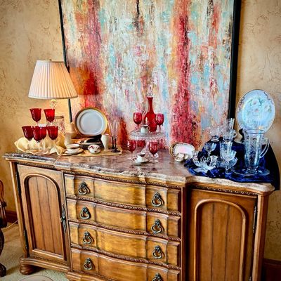 Sale Photo Thumbnail #2: Drexel Heritage sideboard with a marble top, displaying various glassware, china, and a table lamp, set against a large abstract painting.