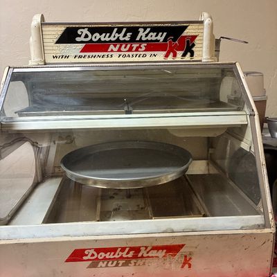 Sale Photo Thumbnail #5: Vintage Double Kay Nuts heated display case, featuring a glass front, metal trays, and original branding graphics, showing some wear and patina from age.