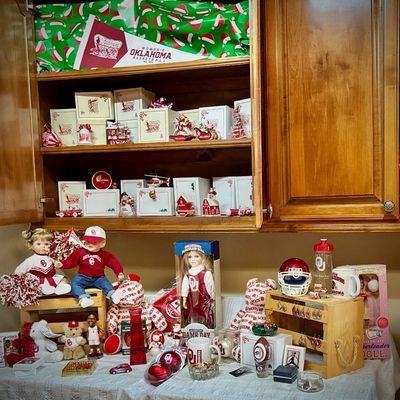 Sale Photo Thumbnail #201: Collection of University of Oklahoma Sooners memorabilia, including collegiate porcelain dolls, plush bears, holiday ornaments, mugs, and a miniature helmet.