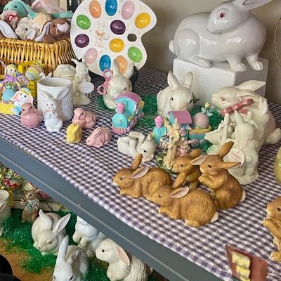 Sale Photo Thumbnail #134: Collection of vintage and contemporary Easter bunny figurines, including ceramic, porcelain, and plush rabbits, displayed on shelves with a purple gingham tablecloth.