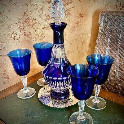 Sale Photo Thumbnail #48: Cobalt blue cut-to-clear crystal decanter with a faceted clear stopper, accompanied by four matching cobalt blue wine goblets with clear twisted stems.