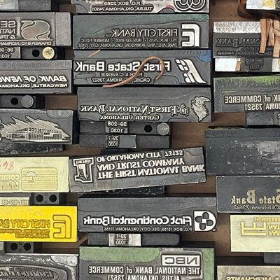 Sale Photo Thumbnail #94: Collection of vintage metal printing blocks and letterpress stamps featuring various Oklahoma bank logos and text.