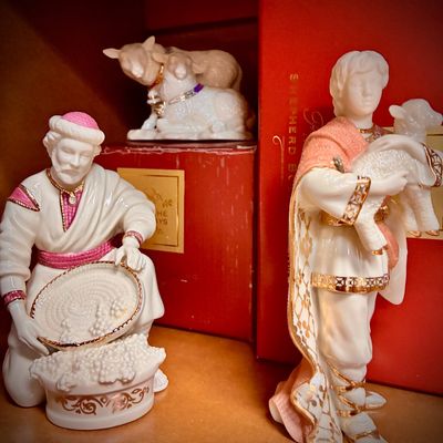 Sale Photo Thumbnail #141: Lenox porcelain nativity figurines, including a kneeling man with a basket, a standing shepherd boy holding a lamb, and a pair of sheep, all featuring gold and pink accents.