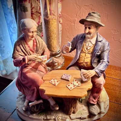Sale Photo Thumbnail #171: Vintage Capodimonte-style porcelain figurine depicting an elderly couple playing cards at a rustic table, featuring detailed hand-painted features and a matte finish.