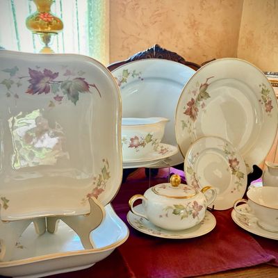 Sale Photo Thumbnail #198: Vintage fine china dinnerware set featuring a delicate autumn leaf pattern with gold-trimmed rims, including plates, bowls, a lidded sugar bowl, and teacups.