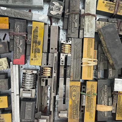 Sale Photo Thumbnail #96: Collection of vintage metal printing blocks and stamps, featuring various business logos and text designs.