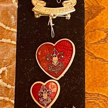 Sale Photo Thumbnail #82: Collection of vintage Boy Scouts of America pins and medals, including "Be Prepared" insignia and heart-shaped mother's pins, displayed on a black velvet stand.