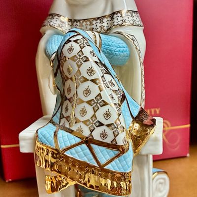 Sale Photo Thumbnail #126: Lenox porcelain figurine depicting a seated scholar or historical figure, featuring intricate gold gilt detailing and light blue accents.