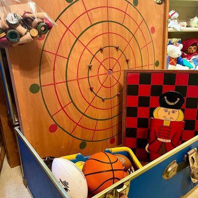 Sale Photo Thumbnail #84: Vintage wooden Carrom board game with game pieces in a plastic bag, displayed alongside a nutcracker-themed checkerboard and a blue toy trunk filled with sports balls.