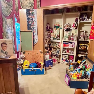 Sale Photo Thumbnail #210: Assorted vintage toys, board games, and plush teddy bears displayed in a closet and on the floor, featuring a Buddy Holly vinyl record and a vintage carrom board.