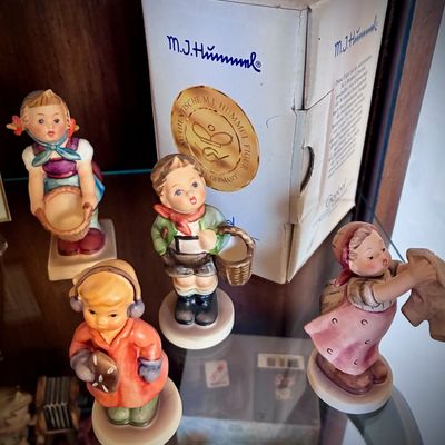 Sale Photo Thumbnail #151: Collection of vintage Goebel Hummel porcelain figurines, including a boy with a basket, a girl hanging laundry, and others, shown with an original box.