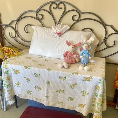 Sale Photo Thumbnail #64: Wrought iron headboard with scrollwork detail, displayed with a floral knit blanket, a white pillow, and two plush Easter bunny dolls.