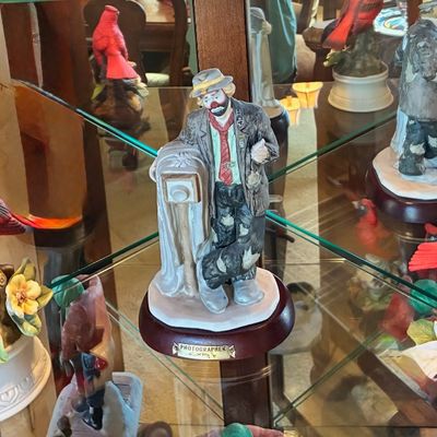 Sale Photo Thumbnail #221: Collection of porcelain figurines displayed on glass shelves, featuring a Ron Lee "Photographer" clown figurine and several detailed cardinal bird figurines perched on branches.