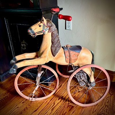 Sale Photo Thumbnail #71: Vintage style carved wood horse tricycle featuring a leather saddle, red painted handlebars, and metal spoked wheels.
