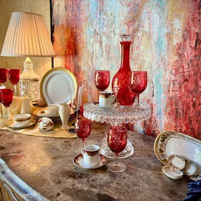 Sale Photo Thumbnail #16: Vintage ruby red glassware collection including a decanter, etched goblets, and wine glasses, displayed alongside fine china, teacups, and a crystal table lamp on a marble-top sideboard.