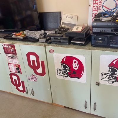 Sale Photo Thumbnail #63: Assorted vintage electronics, including a Sony television, JVC VCR, and Sony cassette deck, displayed on a light green storage cabinet decorated with Oklahoma Sooners decals.