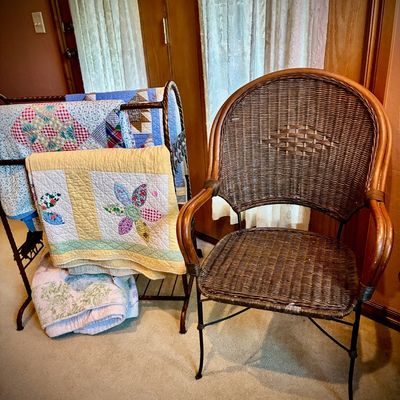 Sale Photo Thumbnail #36: Woven wicker armchair with a metal frame, shown next to a metal quilt rack holding several handmade patchwork quilts.