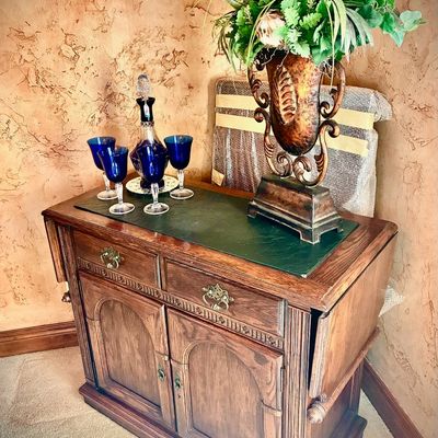 Sale Photo Thumbnail #44: Traditional oak drop-leaf server cabinet with a green leather-insert top, featuring two drawers and two lower cabinet doors with brass hardware.