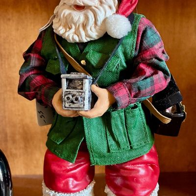 Sale Photo Thumbnail #115: Vintage Santa Claus figurine dressed in a green vest and plaid shirt, holding a miniature vintage camera.