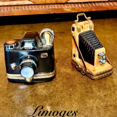 Sale Photo Thumbnail #8: Two vintage Limoges porcelain trinket boxes shaped like cameras, including a black rangefinder style and a classic folding bellows camera, both featuring detailed metal clasps.