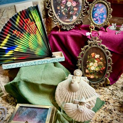 Sale Photo Thumbnail #195: Assortment of vintage decorative items, including ornate brass-framed floral prints, a colorful folding fan, a brass and glass trinket box, and shell-art angel figurines.
