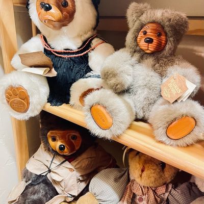 Sale Photo Thumbnail #179: Collection of vintage Raikes Bears featuring carved wooden faces and paws, dressed in various outfits and displayed on wooden shelves.