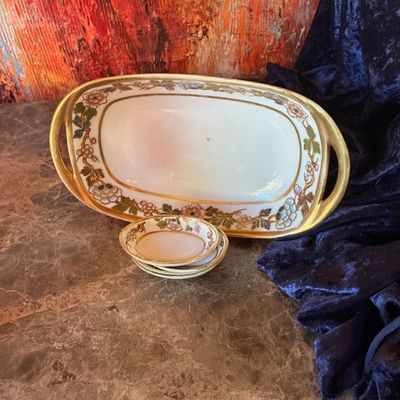 Sale Photo Thumbnail #220: Vintage hand-painted porcelain serving tray with gold-gilt handles and floral borders, accompanied by a matching set of small individual butter or nut dishes.