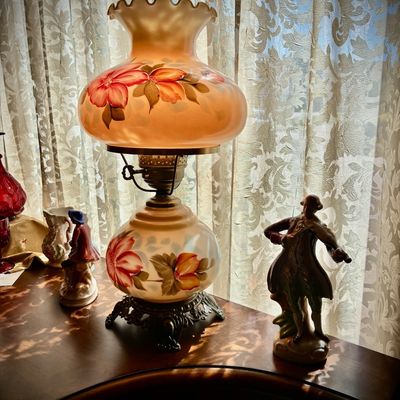 Sale Photo Thumbnail #103: Vintage Gone with the Wind style hurricane lamp featuring hand-painted floral details on a milk glass body, flanked by small porcelain figurines.