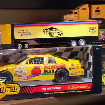 Sale Photo Thumbnail #175: Ertl Collectibles 1:18 scale 1998 Monte Carlo Kodak Max NASCAR die-cast car in its original packaging, shown with Kodak Film racing semi-truck toys.