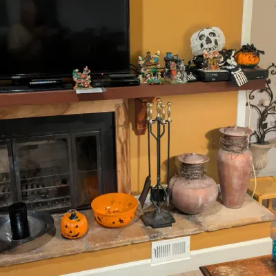 Sale Photo Thumbnail #23: Fireplace hearth display featuring a black metal tool set, two rustic terracotta lidded urns wrapped in twigs, and various Halloween decorations including a jack-o'-lantern bowl and pumpkin figurine.