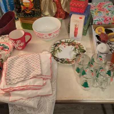 Sale Photo Thumbnail #82: Assortment of Christmas tableware and decorations, including a gold angel tree topper, holiday-themed mugs, plates, linens, and decorative gift boxes.