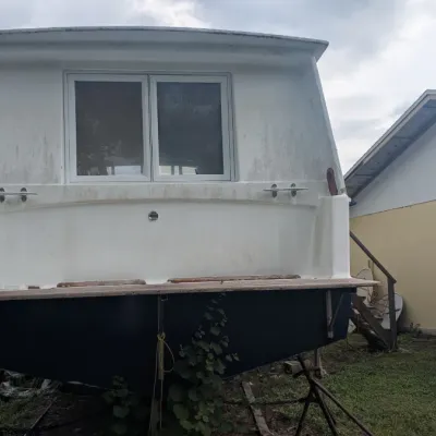 Sale Photo Thumbnail #96: Stern view of a white and blue cabin cruiser boat on jack stands, showing a sliding glass window and swim platform.
