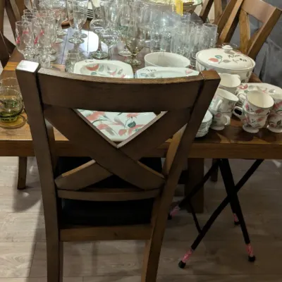 Sale Photo Thumbnail #15: Large collection of vintage glassware and floral-patterned ceramic dinnerware, including Mikasa pieces, displayed on a wooden dining table with cross-back chairs.