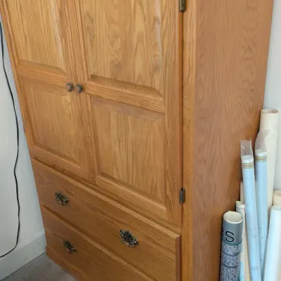 Sale Photo Thumbnail #34: Traditional oak armoire featuring a double-door upper cabinet with raised panels and two lower drawers with ornate brass pulls.