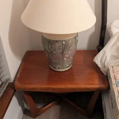 Sale Photo Thumbnail #33: Mid-century modern style wooden end table with an X-base, topped with a textured ceramic table lamp featuring abstract relief patterns.