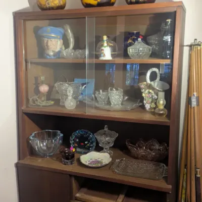 Sale Photo Thumbnail #71: Mid-century modern wooden hutch with sliding glass doors, displaying a collection of vintage glassware, art glass vases, and decorative items.