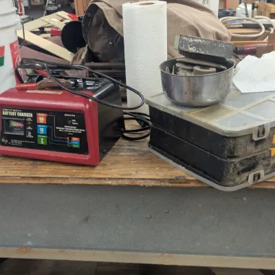 Sale Photo Thumbnail #68: Cen-Tech 2/10/50 Amp 12V manual battery charger with engine start, shown alongside various workshop tools and storage containers on a workbench.