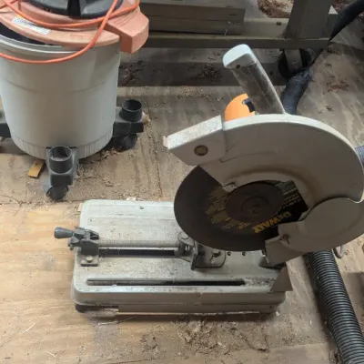 Sale Photo Thumbnail #53: DeWalt chop saw with a metal cutting disc, showing signs of workshop use, alongside a shop vacuum in the background.