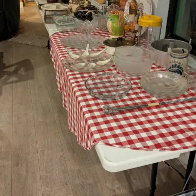 Sale Photo Thumbnail #80: Assorted vintage kitchenware, glassware, and serving dishes displayed on a red-and-white checkered tablecloth over folding tables.