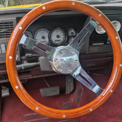 Sale Photo Thumbnail #60: Aftermarket wood-rimmed steering wheel with chrome spokes, installed in a vehicle with a maroon interior.
