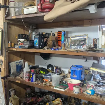Sale Photo Thumbnail #67: Wooden shelving unit filled with various workshop items, including power tools, automotive fluids, a Toro leaf blower, and decorative wooden ship wheels.
