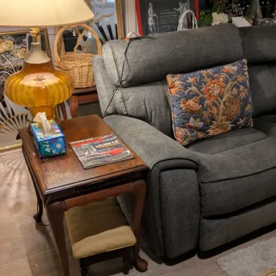 Sale Photo Thumbnail #17: Queen Anne style cherry wood end table with cabriole legs, paired with a vintage amber glass table lamp and a modern charcoal gray reclining sofa.