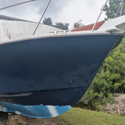 Sale Photo Thumbnail #94: Vintage cabin cruiser boat with a dark blue hull and white upper deck, shown on dry dock supports.