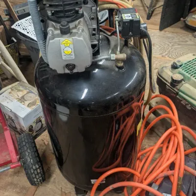 Sale Photo Thumbnail #44: Portable vertical air compressor with a black tank, showing some wear and dust from workshop use, accompanied by an orange air hose.