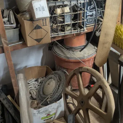 Sale Photo Thumbnail #88: Assorted workshop items, including a large cast iron wheel, a shop vacuum, rope, and various tools on wooden shelving.