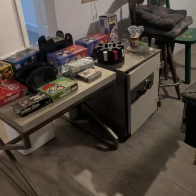 Sale Photo Thumbnail #70: Assorted board games, poker chips, and a heavy-duty home safe displayed on a metal-framed console table.